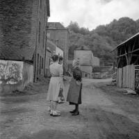  Deux citadines en conversation avec une femme du village. La maison à l'arrière plan est une boulangerie-patisserie
